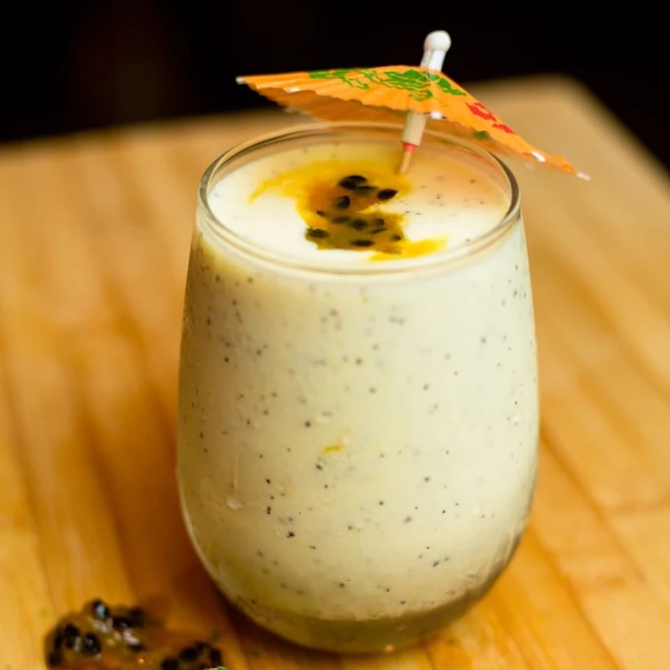 Creamy passion fruit smoothie with seeds and an orange cocktail umbrella on a wooden surface.