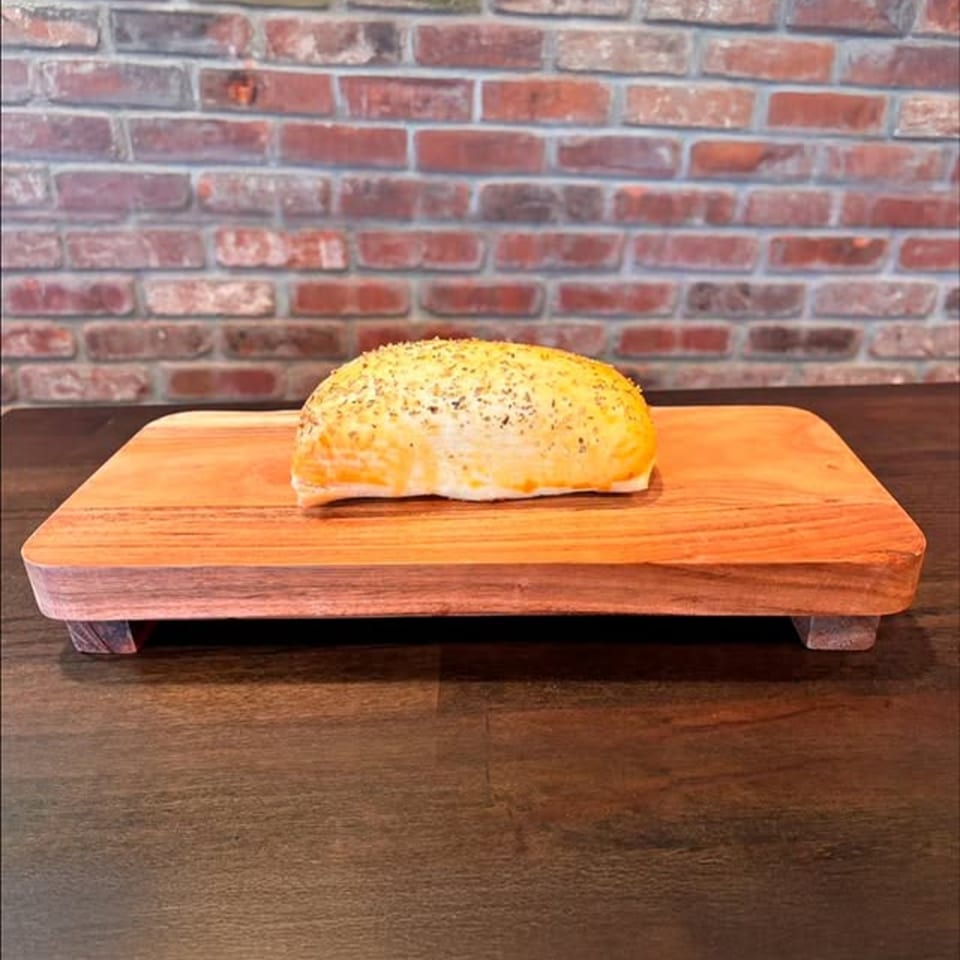 A golden-brown baked pastry, sprinkled with herbs, rests on a wooden serving board.