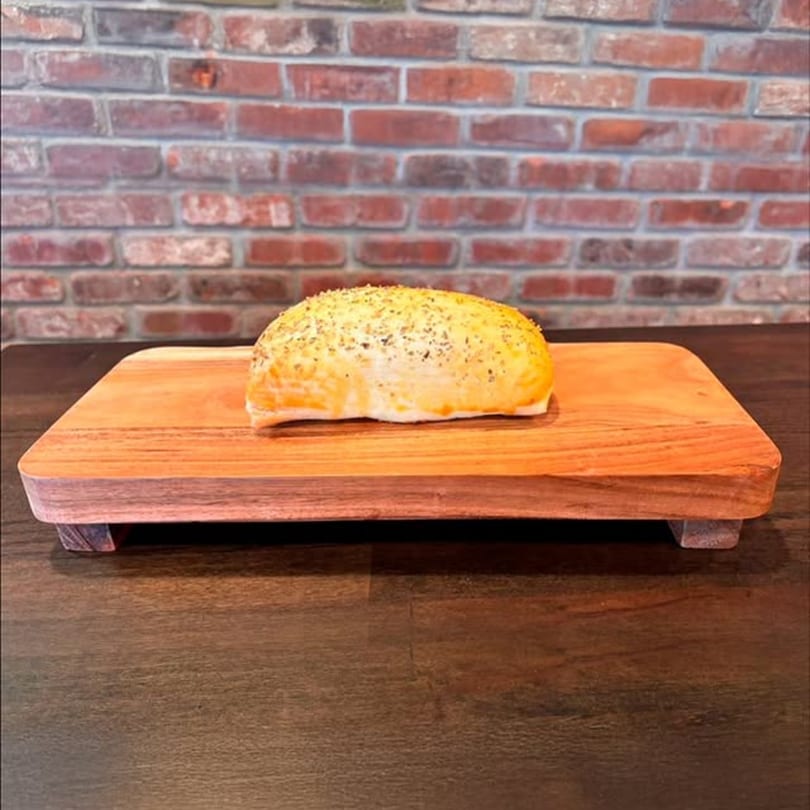 A golden-brown baked pastry, sprinkled with herbs, rests on a wooden serving board.