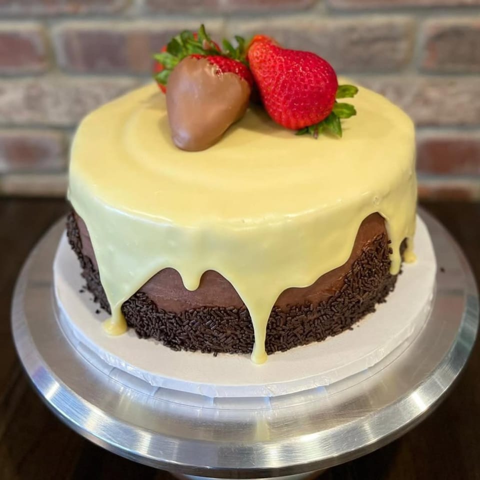 Chocolate cake with white chocolate ganache, chocolate sprinkles, and fresh strawberries on top.